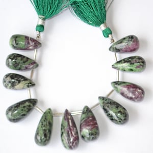 May include: A strand of 10 green, pink, and black gemstone beads. The beads are pear-shaped and have a mottled appearance. The beads are strung on a silver wire.