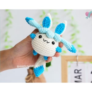 Könnte beinhalten: Ein gehäkeltes Amigurumi-Spielzeug in Form eines blauen und weißen Wesens mit großen Ohren und einem kleinen, runden Körper. Das Spielzeug hat ein süßes, cartoonartiges Gesicht mit schwarzen Augen und einer rosa Nase.