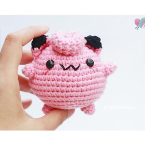 Könnte beinhalten: Ein rosa gehäkeltes Amigurumi-Spielzeug mit schwarzen Ohren und Augen. Das Spielzeug hat ein kleines, gesticktes Lächeln.