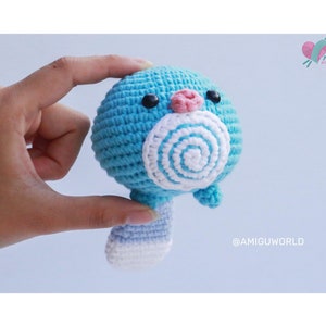 Könnte beinhalten: Ein blaues gehäkeltes Amigurumi-Spielzeug mit einem weißen Spiralmuster auf dem Gesicht und einer rosa Nase. Das Spielzeug hat einen weiß-blauen Schwanz.