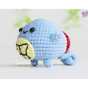 May include: A crocheted blue and yellow amigurumi toy with a red and white striped tail. The toy has a round body and a small, pointed nose. The toy is sitting on a white surface.