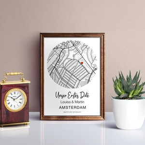 Pu&ograve; includere: Una stampa incorniciata con una mappa di Amsterdam in bianco e nero, un cuore rosso che segna una posizione e il testo "Unser Erstes Date Louisa & Martin AMSTERDAM" sotto la mappa.