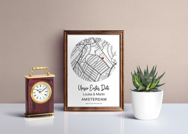 Pu&ograve; includere: Una stampa incorniciata con una mappa di Amsterdam in bianco e nero, un cuore rosso che segna una posizione e il testo "Unser Erstes Date Louisa & Martin AMSTERDAM" sotto la mappa.
