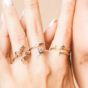 May include: A woman wearing three gold and silver rings with the names "Dylan", "Faith", "Felix", and "Katie" engraved on them.