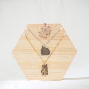 May include: Three necklaces displayed on a wooden hexagonal stand. The top necklace features a rose gold pendant with the names "Rose Emma Troy" engraved on it. The middle necklace has a silver pendant with a cat silhouette. The bottom necklace has a gold pendant with a cat silhouette.