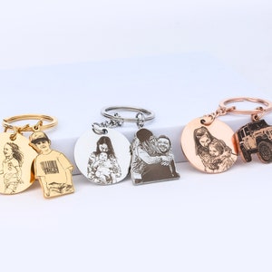Puede incluir: Tres llaveros de plata con imágenes grabadas. El primer llavero tiene un dije redondo dorado con una imagen grabada de una niña. El segundo llavero tiene un dije redondo dorado con una imagen grabada de un niño. El tercer llavero tiene un dije redondo de color oro rosa con una imagen grabada de una mujer y una niña, y un dije redondo de color oro rosa más pequeño con una imagen grabada de un jeep.