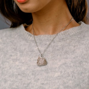 May include: A silver chain necklace with a pendant featuring a detailed engraved image of a cat's face.