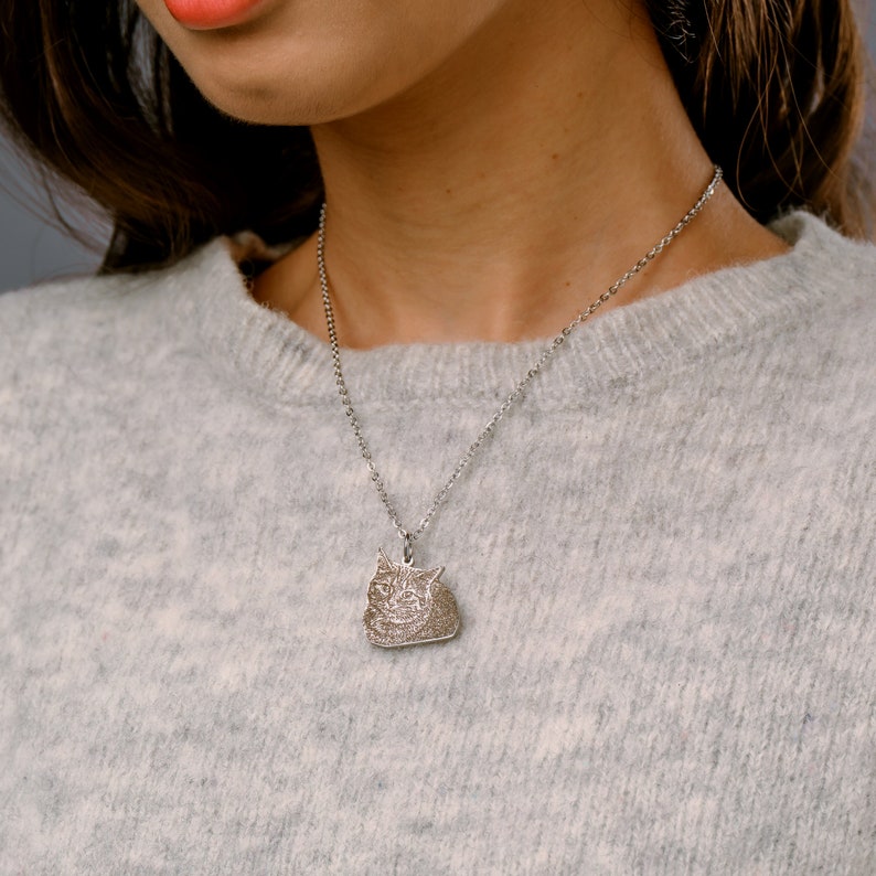 May include: A silver chain necklace with a pendant featuring a detailed engraved image of a cat's face.