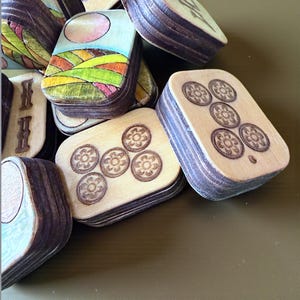 Handmade wooden Riichi Mahjong tiles featuring a colorful sunrise design with pink sun and rolling hills.
