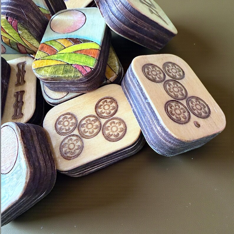 Handmade wooden Riichi Mahjong tiles featuring a colorful sunrise design with pink sun and rolling hills.