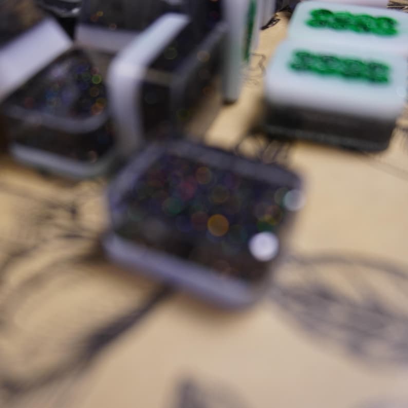 May include: Close-up of several black and white game tiles with green markings. Some tiles have a glittery, iridescent appearance. The tiles are arranged on a light-colored surface, possibly a game board.