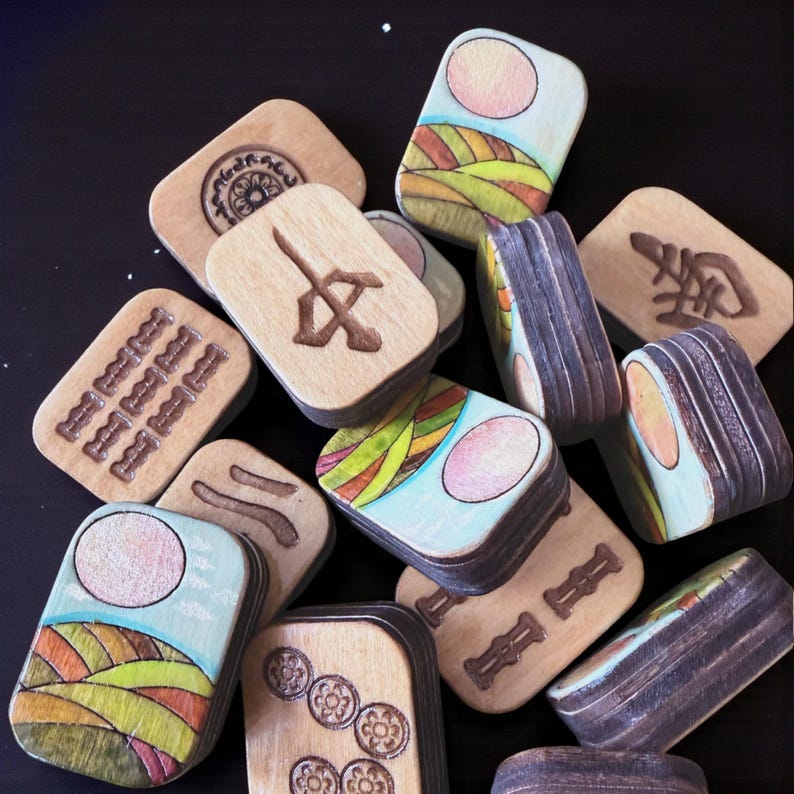 Handmade wooden Riichi Mahjong tiles featuring a colorful sunrise design with pink sun and rolling hills.