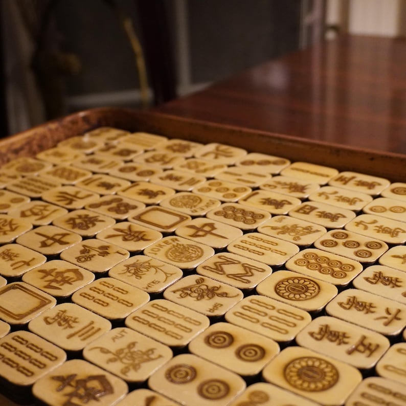Handcrafted wooden Mahjong tiles with engraved Riichi symbols arranged neatly on a tabletop.