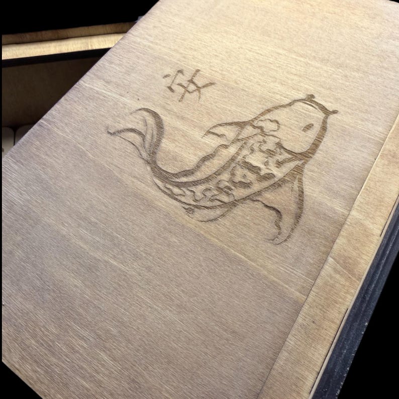May include: Wooden box with a detailed etched design of a koi fish and a Japanese character. The fish is centered on the lid, with the character above it. The wood has a natural, light brown color.