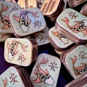 Finished Koi Fish Riichi Mahjong tiles handcrafted from layered wood and engraved using an xTool laser engraver.
