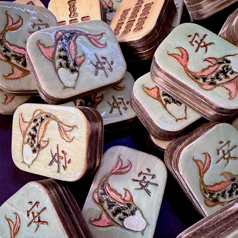 Finished Koi Fish Riichi Mahjong tiles handcrafted from layered wood and engraved using an xTool laser engraver.