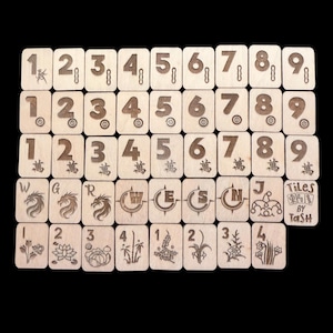 May include: A set of wooden tiles, each engraved with numbers, symbols, and illustrations. The tiles display numbers 1-9, Chinese characters, and various images. The text "Tiles by Tash" is also visible.