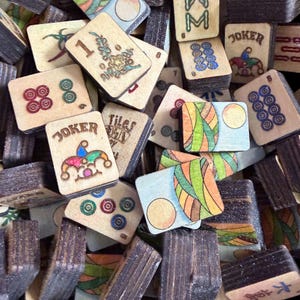 Puede incluir: Una colecci&oacute;n de fichas de Mahjong de madera vintage. Las fichas presentan varios dise&ntilde;os, incluyendo n&uacute;meros, palos y cartas de comod&iacute;n. Las fichas son en tonos marr&oacute;n, beige y presentan acentos coloridos. La imagen muestra una vista de cerca de las fichas.