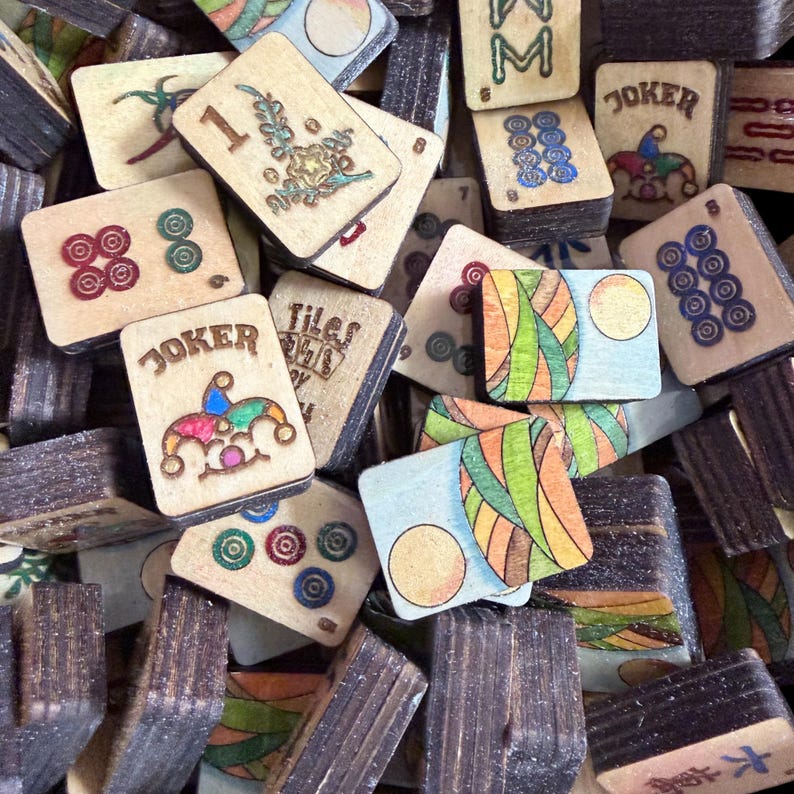 Puede incluir: Una colecci&oacute;n de fichas de Mahjong de madera vintage. Las fichas presentan varios dise&ntilde;os, incluyendo n&uacute;meros, palos y cartas de comod&iacute;n. Las fichas son en tonos marr&oacute;n, beige y presentan acentos coloridos. La imagen muestra una vista de cerca de las fichas.