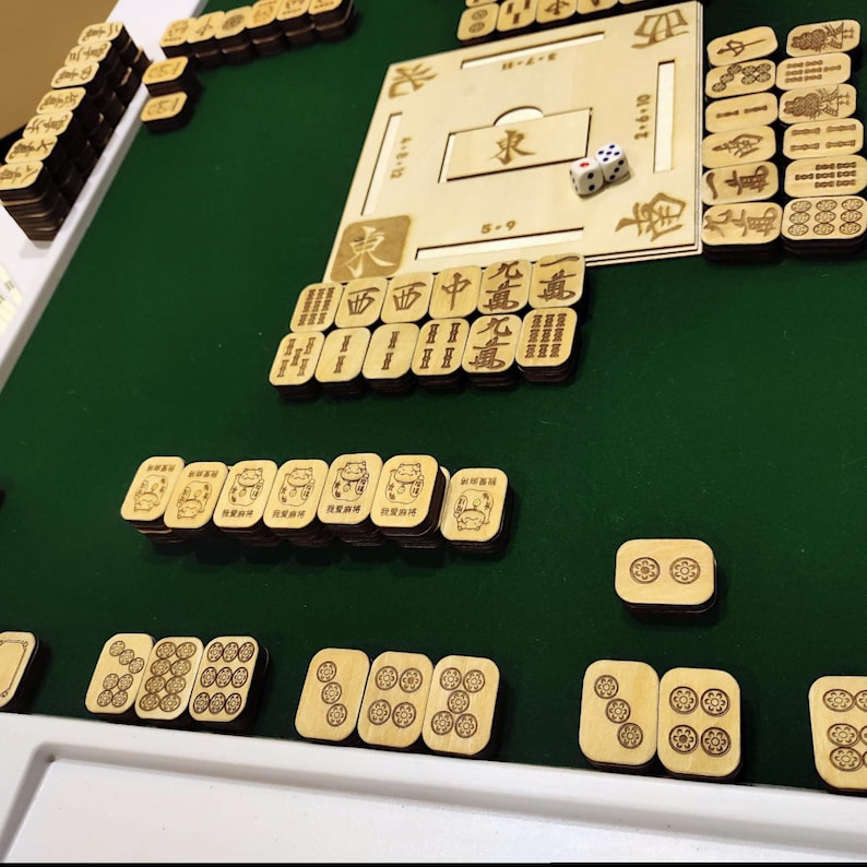 May include: A wooden Mahjong set with a green felt playing surface. The set includes wooden tiles with engraved characters and symbols, a wooden board, and dice. The tiles are arranged in stacks and rows, ready for play.