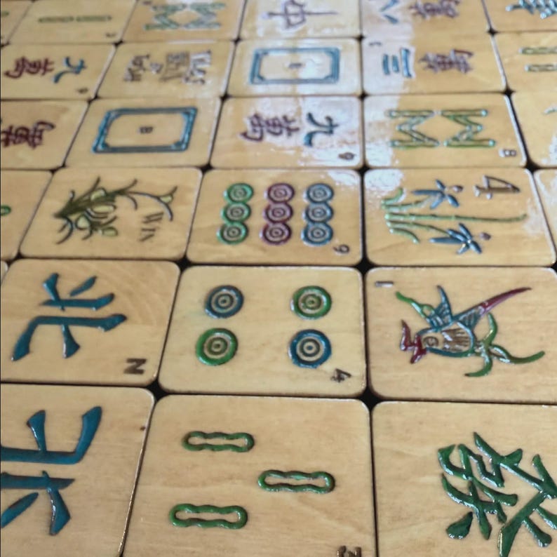 May include: A close-up shot of a set of wooden Mahjong tiles. The tiles display diverse symbols and characters in blue, green, and red. The tiles are arranged in a grid, displaying the game's components.