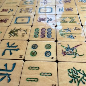 Puede incluir: Primer plano de una colecci&oacute;n de fichas de Mahjong de madera. Las fichas presentan varios s&iacute;mbolos y caracteres en verde, azul y rojo. Las fichas est&aacute;n dispuestas en un patr&oacute;n de cuadr&iacute;cula, mostrando los detalles de las piezas del juego.