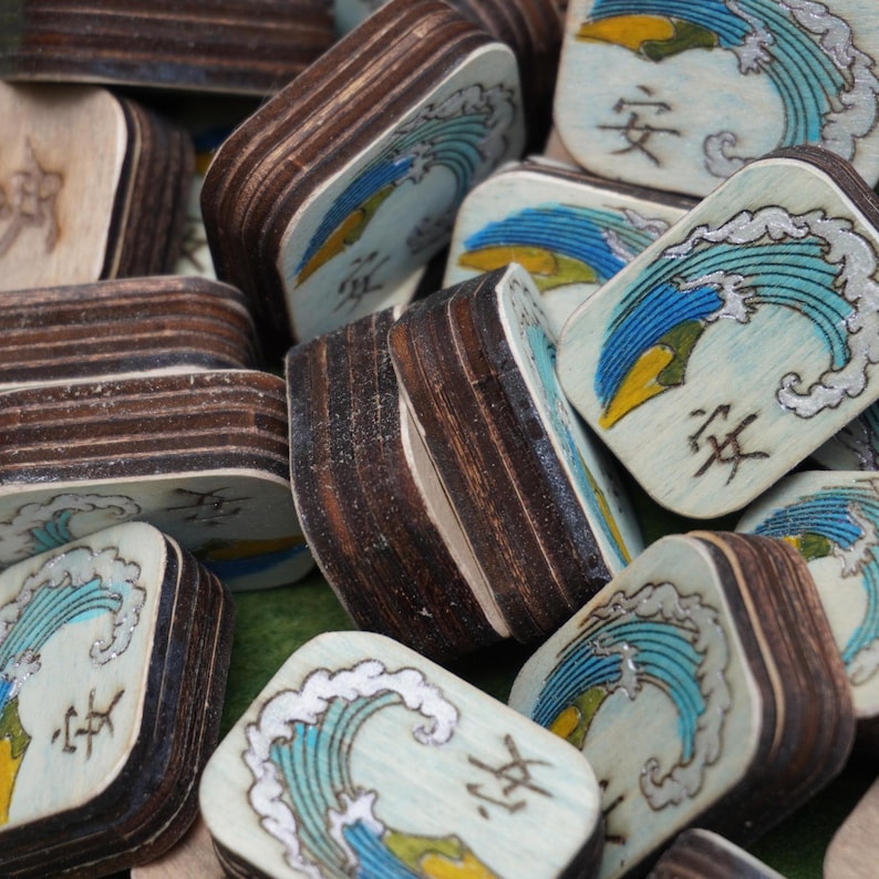 Puede incluir: Posavasos de madera con dise&ntilde;o de olas en azul, amarillo y plateado. Cada posavasos tiene un borde marr&oacute;n oscuro y un car&aacute;cter japon&eacute;s. Los posavasos est&aacute;n apilados y dispersos.