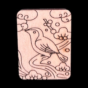May include: A rectangular wooden carving featuring a bird perched on a branch, surrounded by stylized clouds and foliage. The design is etched in black against the light wood grain, creating a contrasting effect. The overall aesthetic is reminiscent of traditional woodblock prints.