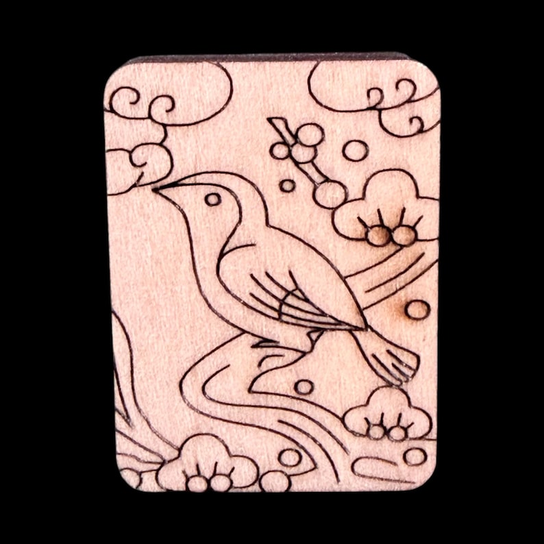 May include: A rectangular wooden carving featuring a bird perched on a branch, surrounded by stylized clouds and foliage. The design is etched in black against the light wood grain, creating a contrasting effect. The overall aesthetic is reminiscent of traditional woodblock prints.