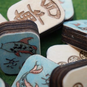 May include: Close-up of wooden tiles with painted fish and Chinese characters. The tiles have a light blue background with red and black fish illustrations. The edges of the tiles are dark brown.