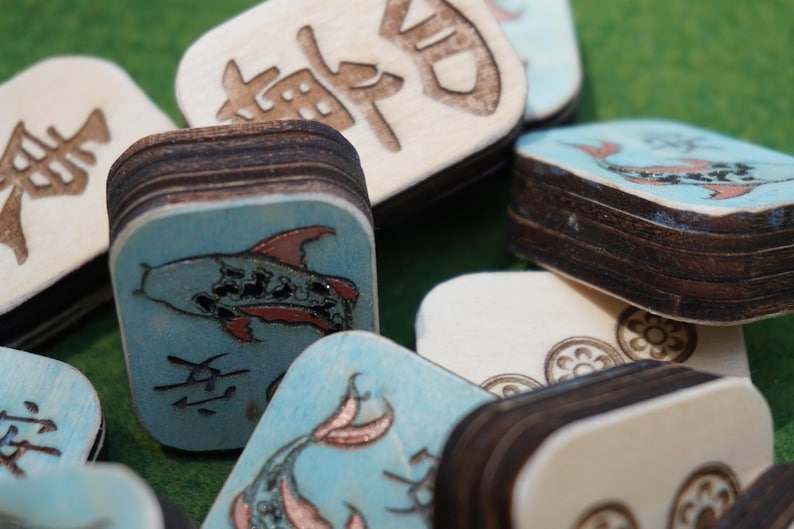 May include: Close-up of wooden tiles with painted fish and Chinese characters. The tiles have a light blue background with red and black fish illustrations. The edges of the tiles are dark brown.