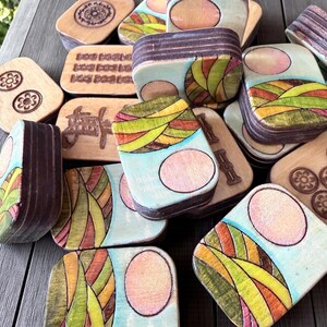 Handmade wooden Riichi Mahjong tiles featuring a colorful sunrise design with pink sun and rolling hills.
