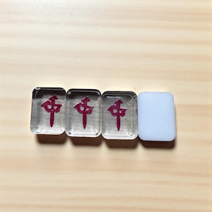 May include: Four clear rectangular Mahjong tiles. Three tiles have a red Chinese character. The fourth tile is white. The tiles are on a light wood surface.
