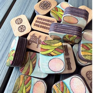 Handmade wooden Riichi Mahjong tiles featuring a colorful sunrise design with pink sun and rolling hills.
