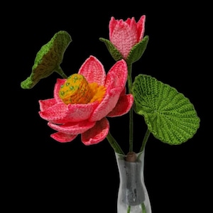 May include: A crocheted bouquet of pink lotus flowers with green leaves in a clear glass vase.
