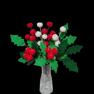 May include: A crocheted bouquet of red and white berries with green leaves in a clear glass vase.