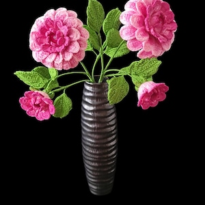 May include: A bouquet of crocheted pink flowers with green leaves in a black vase.