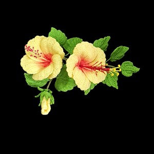 May include: Two crocheted yellow hibiscus flowers with red centres and green leaves. The flowers are attached to a stem with a small bud.
