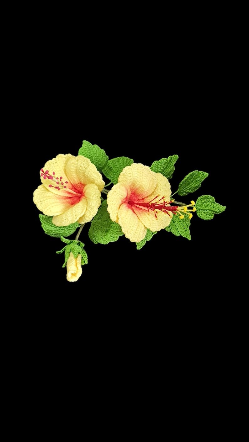 May include: Two crocheted yellow hibiscus flowers with red centres and green leaves. The flowers are attached to a stem with a small bud.