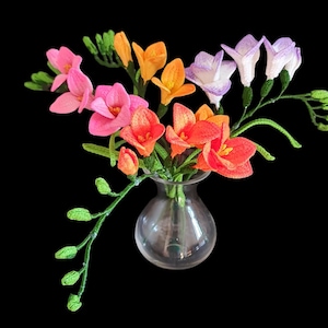 May include: A bouquet of colorful freesia flowers in a clear glass vase. The flowers are pink, orange, and purple.