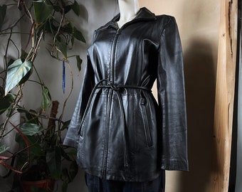May include: A black leather jacket with a belted waist and a zipper closure. The jacket has a stand-up collar and long sleeves.