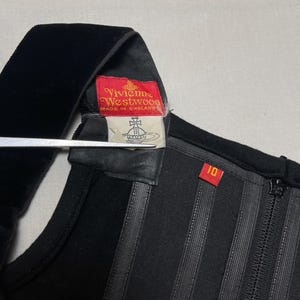 May include: Close-up of a black garment with a velvet strap. A red tag with "Vivienne Westwood" and "MADE IN ENGLAND" is visible. The garment has vertical striped detailing and a size 10 tag.