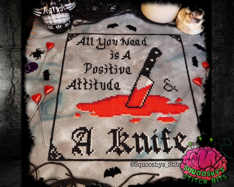 May include: Cross stitch pattern with a black and white design of a knife with red blood dripping from it. The text reads "All you need is a positive attitude & a knife".