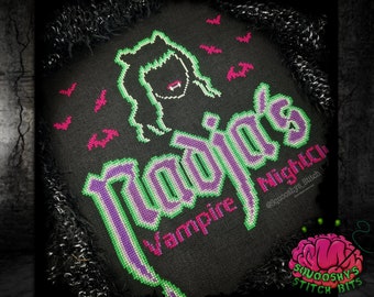 May include: Cross stitch pattern of a vampire with fangs and long hair, with the text "Radja's Vampire Nightclub" in a gothic font. The pattern is stitched on black fabric with green and purple thread.