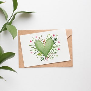 May include: A brown envelope with a white card inside. The card features a green heart surrounded by green leaves and pink flowers.