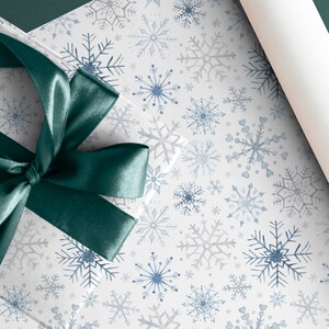 May include: A white gift box with a teal satin ribbon tied in a bow. The box is wrapped in white paper with a blue and gray snowflake pattern.