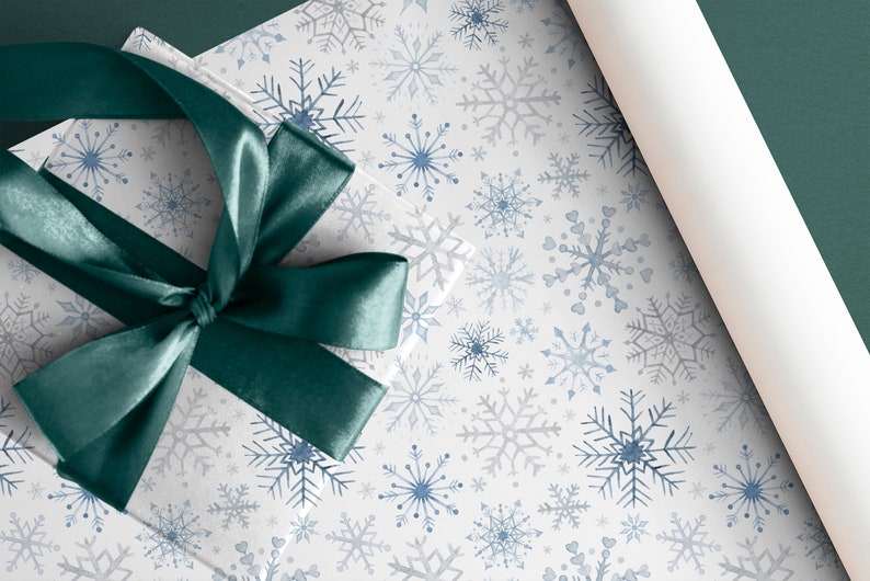 May include: A white gift box with a teal satin ribbon tied in a bow. The box is wrapped in white paper with a blue and gray snowflake pattern.