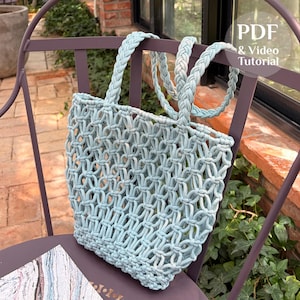 May include: A light blue macrame tote bag featuring an open-weave knotted pattern and two braided handles. The bag includes a circular overlay with the text PDF & Video Tutorial. The design consists of interconnected cord loops forming a grid.