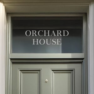 Könnte beinhalten: Eine grüne Holztür mit einem Glaseinsatz darüber. Der Glaseinsatz trägt die Aufschrift "Orchard House" in weißen Buchstaben. Die Tür hat einen Türklopfer aus Messing und ein Messing-Namensschild mit der Aufschrift "Liverpoool".