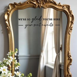 May include: A gold-framed mirror with a black vinyl decal that reads "We're so glad you're here - your seat awaits - "